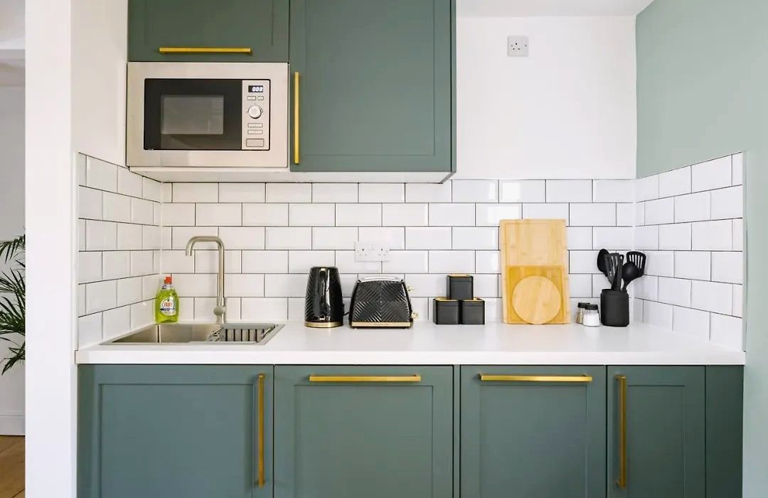 Kitchenette with green cabinets and brass handles